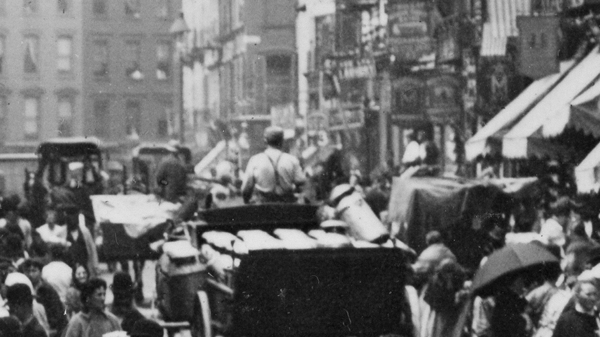Another enlarged section of the first photo. A man is driving a horse drawn cart, filled with milk jugs, down the street. He is surrounded on all sides by people shopping.